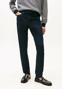 Donkerblauwe denim jeans met een slim fit, voorzien van een klassiek vijf-pocket ontwerp en een subtiele, gestructureerde afwerking, gecombineerd met zwarte instappers.