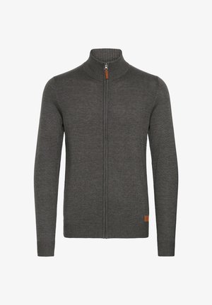 Sweat-shirt zippé gris avec un col haut, texture côtelée, et un petit accent en cuir en bas à gauche. Manches longues et design ajusté.