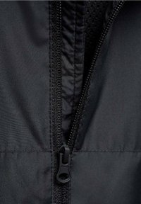 Detalj av svart jackdragkedja med texturerat tyg. Har en svart dragkedjebana och dragflik som framhäver låsmekanismen.