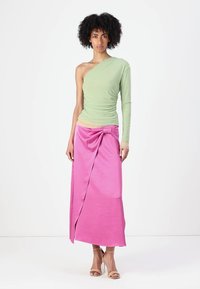 Green one-shoulder top with ruched detail paired with a pink wrap skirt featuring a bow accent, showcasing soft fabrics and contrasting colors.