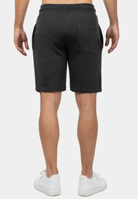 Zwarte katoenen shorts met een relaxte pasvorm, voorzien van een achterzak en zijnaden. Gecombineerd met witte sneakers.