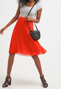 Plisserad röd kjol med en utställd form, kombinerad med en randig svart- och vit topp och en liten svart axelväska. Svarta klacksandaler.