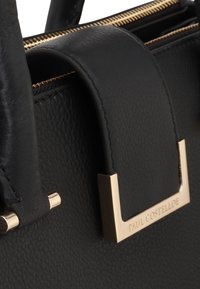 Zwarte leren handtas met een gestructureerde oppervlakte, voorzien van gouden hardware en een prominente merkplaat. Ritsdetail aan de bovenkant.