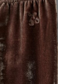 Ruskea samettikangas, jossa on pehmeä pinta, ylhäällä kootut joustimet ja pieni kirsikkakirjonta sivussa.