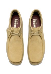 Ruskindørk støvler i lys beige med firkantet tå, rundede snørebånd og en struktureret overflade. Indersiden har en maroon indlægssål med "Clarks ORIGINAL" tryk.
