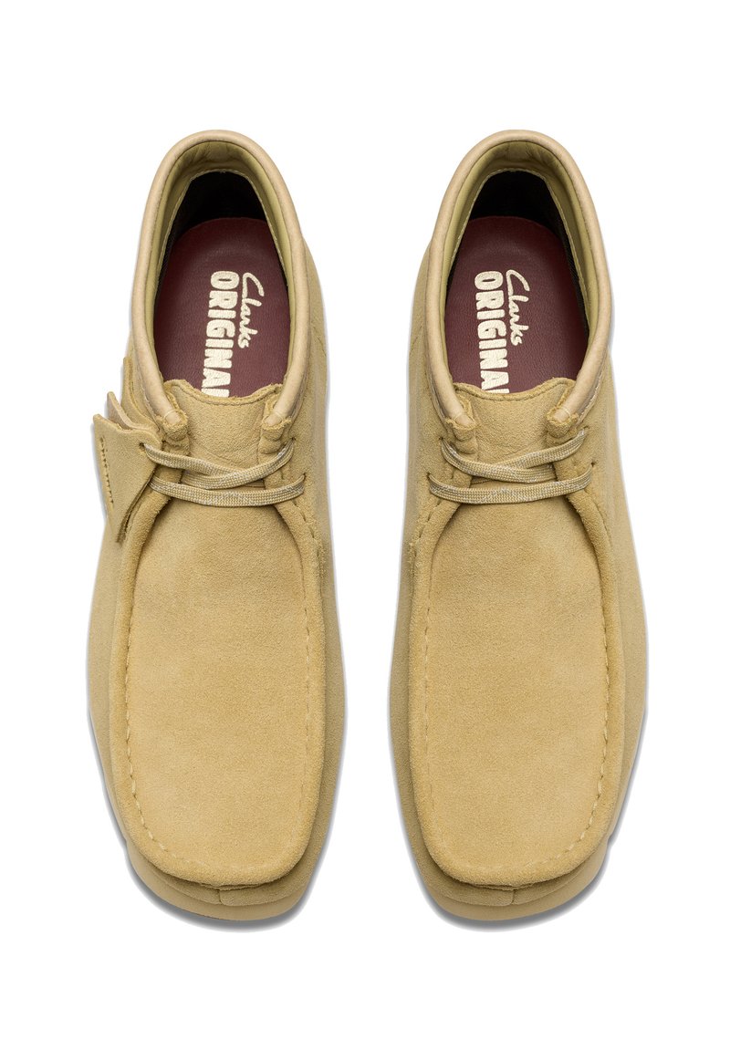 Suede desert boots in light beige with a square toe, rounded laces, and a textured surface. Inside has a maroon insole with "Clarks ORIGINAL" lettering.