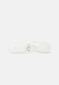 Semelle de chaussure transparente et plate avec une surface texturée antidérapante et un petit talon, photographiée par le dessous sur un fond blanc.