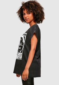 Čierne oversized tričko vyrobené z bavlny s krátkymi rukávmi s odrolovaním, so grafickým dizajnom na prednej strane, ktorý hovorí "Je to môj rok '86, zlatko."