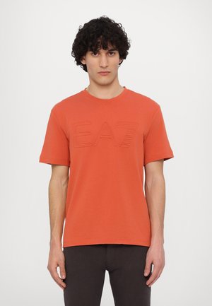 Red cotton t-shirt with short sleeves, featuring an embossed "EA7" logo on the front and a crew neckline. Smooth texture, relaxed fit.
