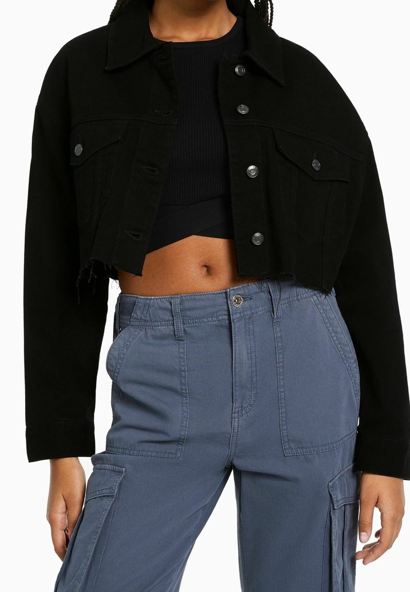 Svart kort denimjacka med knäppning, oversized passform och framfickor. Kombinerad med blå cargo-byxor med sidfickor.