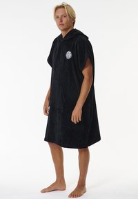 Poncho asciugamano nero con cappuccio, realizzato in morbido tessuto di spugna, dotato di una tasca frontale e di un logo circolare sul petto.