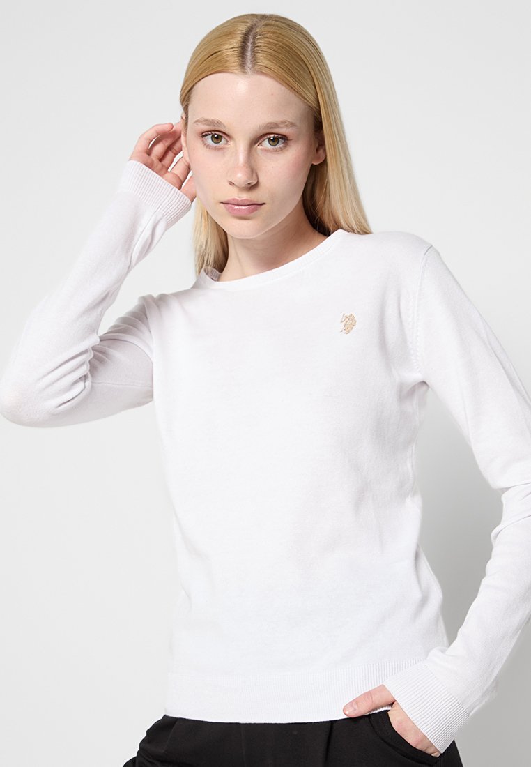 Weißer Longsleeve-Pullover mit rundem Halsausschnitt, gerippten Bündchen und einem kleinen goldenen Emblem auf der Brust. Weicher Strickstoff mit glatter Textur.