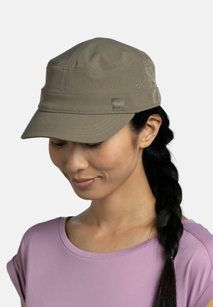 Mujer con cabello largo trenzado, que lleva una gorra marrón claro y una camisa morada clara, mirando hacia abajo con una leve sonrisa.