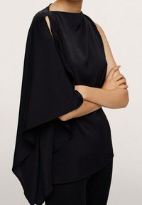 Haut asymétrique noir avec une manche drapée d'un côté, en tissu lisse, présentant un col rond et une coupe décontractée.