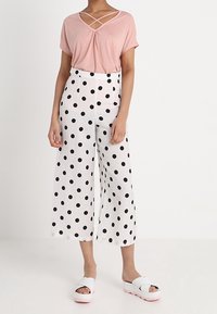 Lyserød T-shirt med korte ærmer og krydsnakket, parret med hvide culottes med sorte prikker og hvide platform sandaler med lyserøde såler.