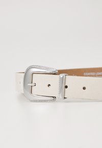 Ceinture en cuir enduit de couleur blanc cassé, dotée d'une boucle en argent texturée. Conçue avec plusieurs trous pour un ajustement. Fini de surface lisse.