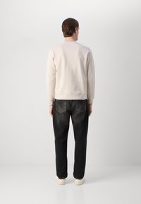 Felpa beige chiaro a girocollo, vestibilità rilassata; abbinata a jeans scuri a gamba affusolata con tasche posteriori. Le scarpe sono beige con una suola testurizzata.