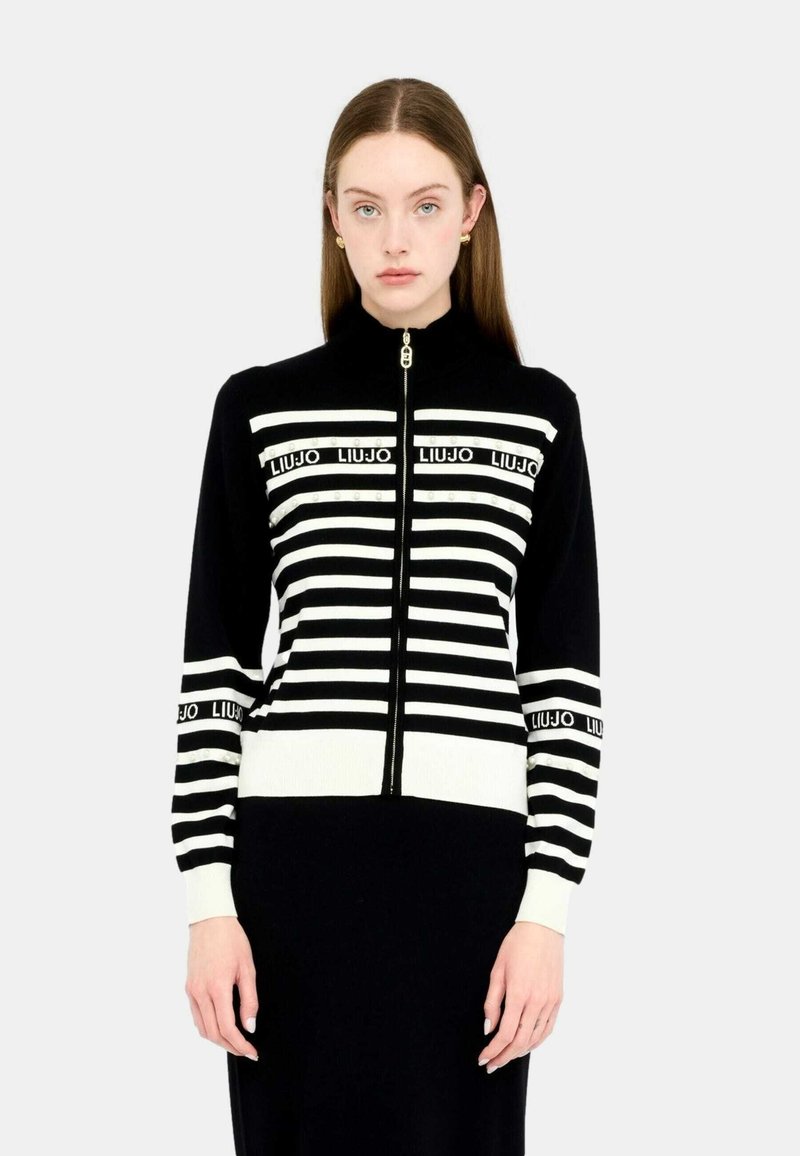 Maglione zip-up a righe bianche e nere con colletto alto. Presenta dettagli con logo e polsini a coste. Morbido materiale a maglia con design aderente.