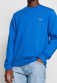 Sudadera azul de mezcla de algodón, con cuello redondo, puños acanalados y acabado texturizado. Pequeño logotipo bordado en el pecho.