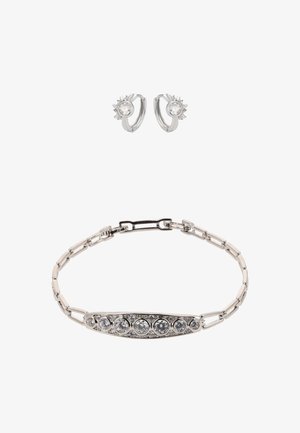 Hopeinen rannekoru, jossa ovaalimainen keskiosa ja pyöreitä, kirkkaita kiviä sekä linkitetty ketju. Mukana hopeiset rinkkorenkaat, joissa on kimaltava keskiosa.