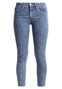Jeans de mezclilla azul ajustados con cintura alta, cierre de botón y diseño clásico de cinco bolsillos. Presenta un ligero desgaste y una textura suave.