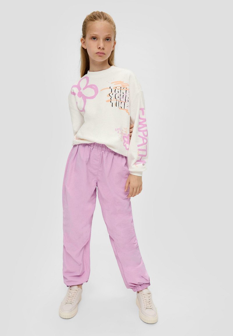 Weißer Sweatshirt mit rosa Blumenmotiven und Text, kombiniert mit lockeren, helllila Hosen. Das Outfit wird mit beigen Sneakers abgerundet.