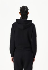 Sudadera de algodón negra con una gran capucha, que presenta franjas laterales texturizadas. Acompañada de pantalones negros a juego.