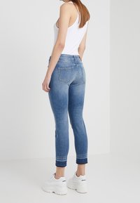 Úzké džíny v světle modrém denimovém odstínu se zesvětlením, s pěti kapsami a ohrnutými manžetami. V kombinaci s bílými teniskami a bílým tílkem.