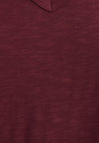 Maroon v-neck shirt made of textured fabric; features subtle horizontal lines and stitched detailing around the neckline.