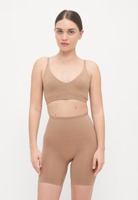 Beige seamless bralette with adjustable straps, paired with high-waisted shorts in the same color; smooth texture and form-fitting design.