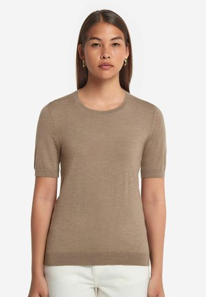 Beige kortærmet strikbluse med rund halsudskæring, ribbede kanter og en glat tekstur, båret over hvidt stof.