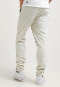 Ljusgrå joggerbyxor i mjukt, strukturerat tyg. Har elastisk midja, sidofickor och smalnande muddar. Utsmyckad med subtila ränder.