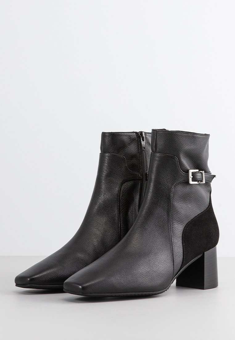 Zwarte enkellaarzen van soepel leer en suède, met een spitse neus, blokhak en een decoratieve zilveren gesp rond de enkel.