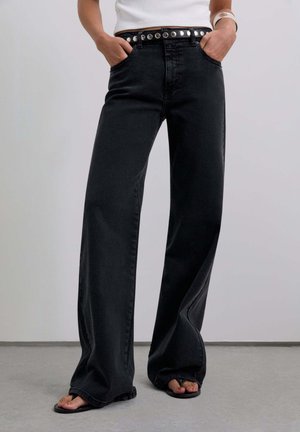 Jean en denim noir à jambes larges avec une taille haute, doté d'une ceinture cloutée argentée, d'une texture lisse et de poches latérales.