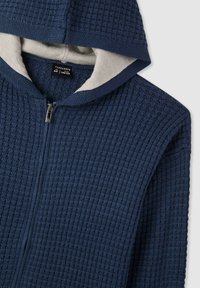 Felpa con cappuccio blu navy con cerniera, caratterizzata da un design a coste testurizzato, con una fodera interna grigio chiaro a contrasto e una chiusura frontale con cerniera.