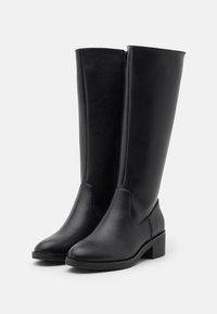 Bottes noires en cuir jusqu'au genou avec une pointe ronde, un talon plat et une fermeture éclair sur le côté, présentant une texture lisse et un design minimal.