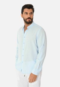 Camicia button-up azzurro chiaro realizzata in lino, con colletto alla mandarino, maniche lunghe e una texture sottile. I bottoni sono dello stesso colore.