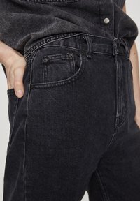 Jean en denim noir à coupe ajustée, taille haute et style classique à cinq poches. Présente un léger effet délavé et une couture contrastante.