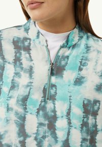 Leichte Zip-up-Top mit einem türkis- und grau gefärbten Batikmuster, einem Stehkragen und einem metallischen Reißverschlussdetail.