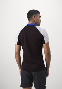 Korte mouwen sportshirt in donkerbruin met witte en blauwe accenten, voorzien van een gestructureerde stof en een klassieke kraagontwerp.