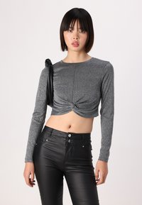 Srebrni metalni crop top dugih rukava s dizajnom uvijenog prednjeg dijela. Uparen s prilagođenim crnim kožnim hlačama s dva gumba.