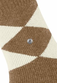 Calzino a maglia argyle marrone e bianco con un piccolo etichetta metallica rotonda vicino al centro.