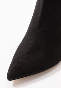 Černá špičatá bota s textilním svrškem. Hladké okraje a přiléhavý design vytvářejí elegantní vzhled.