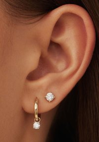Boucle d'oreille en or avec un petit zircon cubique pendent à côté d'une puce d'oreille mettant en avant un zircon cubique plus grand. Les deux sont montés en or.
