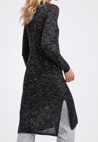 Musta pitkähiha tunika, jossa on teksturoitu, ribattu kuosi valkoisilla pisteillä; sivuaukot helman kohdalla tarjoavat lisäliikkumatilaa.