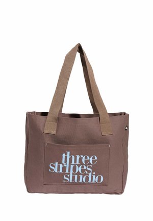 Borsa in tessuto marrone con manici larghi e tasca frontale con la scritta "three stripes studio" in testo azzurro chiaro.