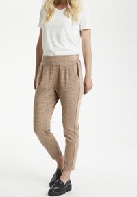 Beige rutiga byxor med en smal passform, med dragsnöre i midjan och sidofickor, kombinerat med en enfärgad vit t-shirt och svarta loafers.