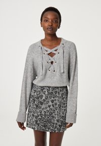Grauer Strickpullover mit Schnürdesign und metallischen Ösen, kombiniert mit einem kurzen Rock im grau-schwarzen Leopardenmuster.