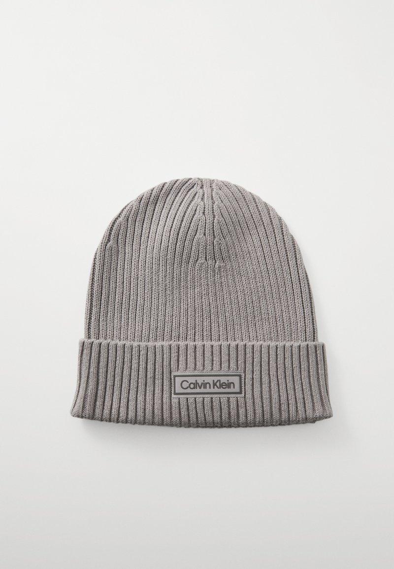 Grijze gebreide beanie met ribbeltextuur, voorzien van een omgeslagen manchette en een rechthoekig logo-patch met "Calvin Klein" in het wit.