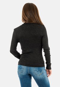 Maglione nero, strutturato, con maniche lunghe, vestibilità slim e filati metallici. Abbinato a jeans blu con un design decorativo della tasca.